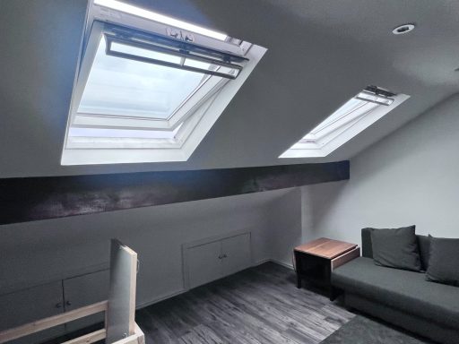 Bright room with slanted ceiling and skylights, featuring a grey sofa and dark flooring.
